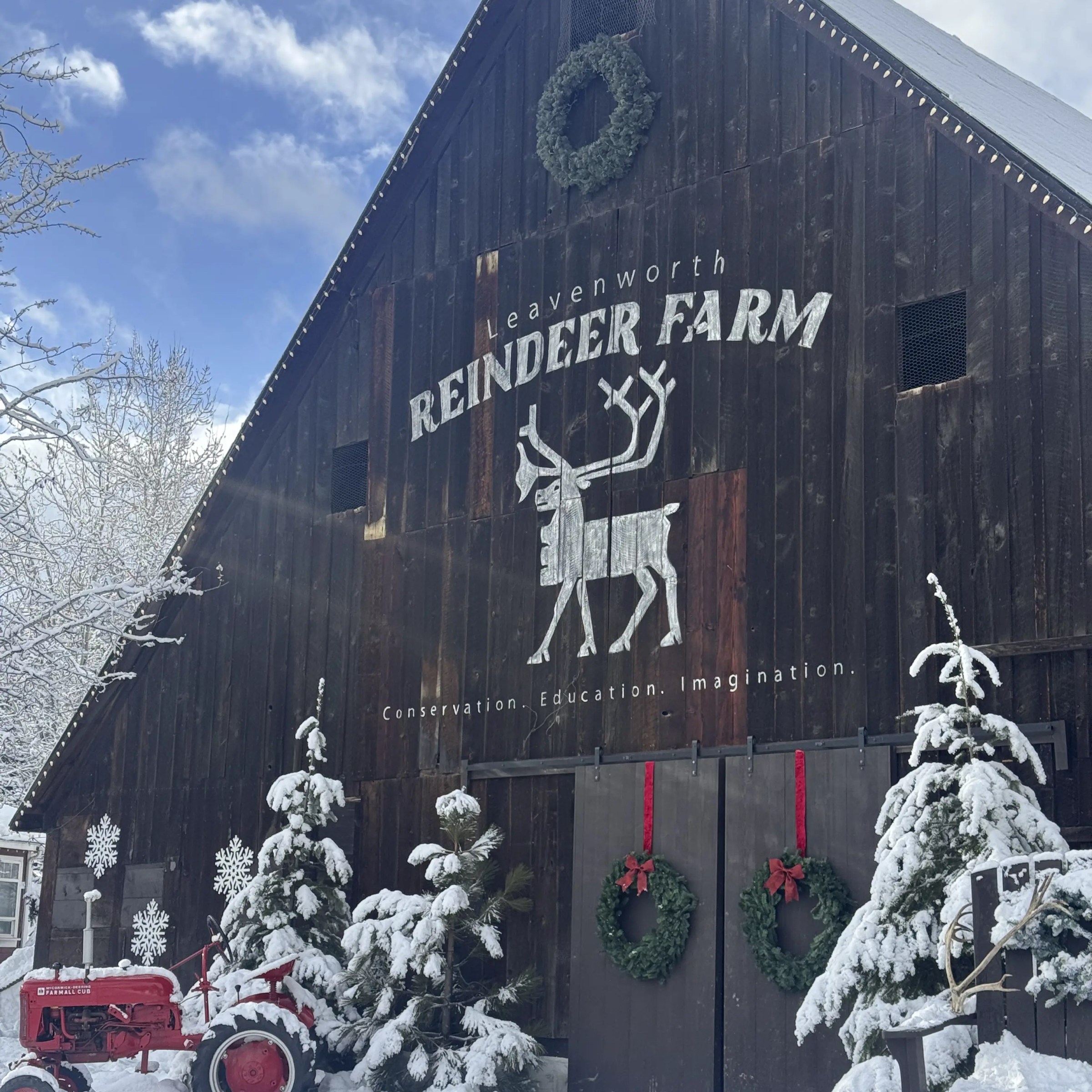 Wooden barn labeled 'Reindeer Farm' with snow-covered trees and a red tractor in front.